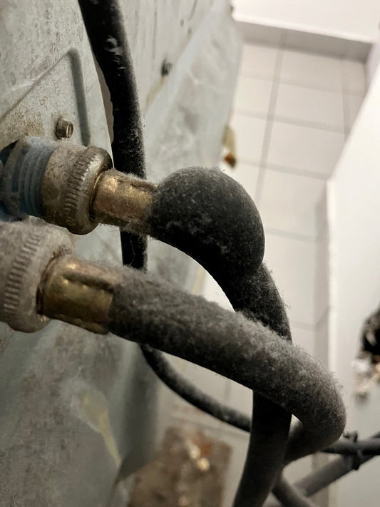 Black rubber washing machine hose with a large bulge near the metal crimp. The bulge looks stretched and weak, showing signs it might burst soon from pressure or damage at the crimp.