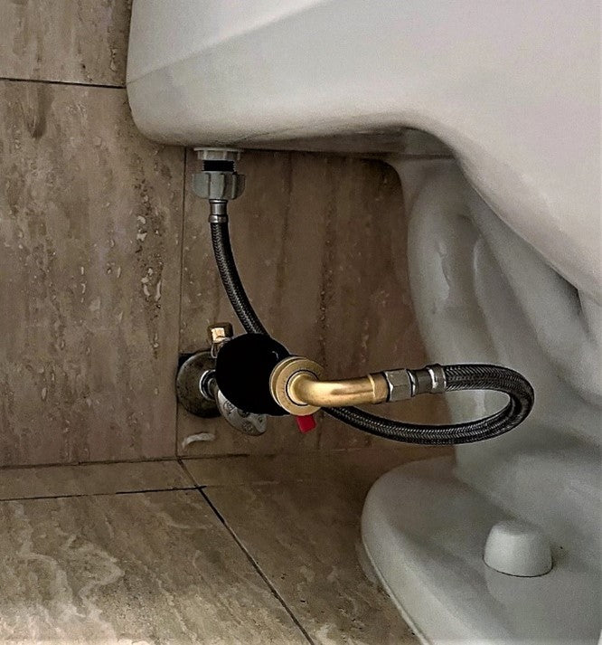 Image of a toilet water leak shutoff kit installed on a toilet. The water block is used to stop the flow of water to the toilet in the event of a leak. The water block reset device is used to reset the water block after a leak has been repaired. The brass adapter is used to connect the water block to the toilet's water supply line. Water shutoff kit is installed in a horizontal orientation. This installation is in a Trump Tower apartment unit in New York City.