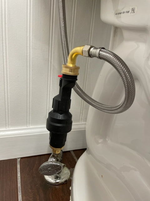 Image of a toilet with a water block kit installed. The kit includes a water block, a water block reset device, and a brass adapter. The water block is used to stop the flow of water to the toilet in the event of a leak. The water block reset device is used to reset the water block after a leak has been repaired. The brass adapter is used to connect the water block to the toilet's water supply line. The device installed on a toilet water line in a vertical orientation.